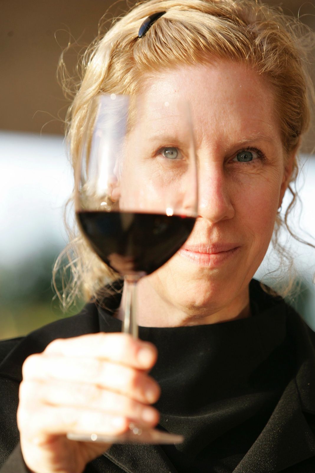 Carina Cooper, sommelier, segurando uma taça de vinho tinto diante do rosto